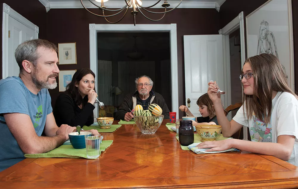 A blended family sits around a dinner table in a bright kitchen, talking calmly and listening to each other.