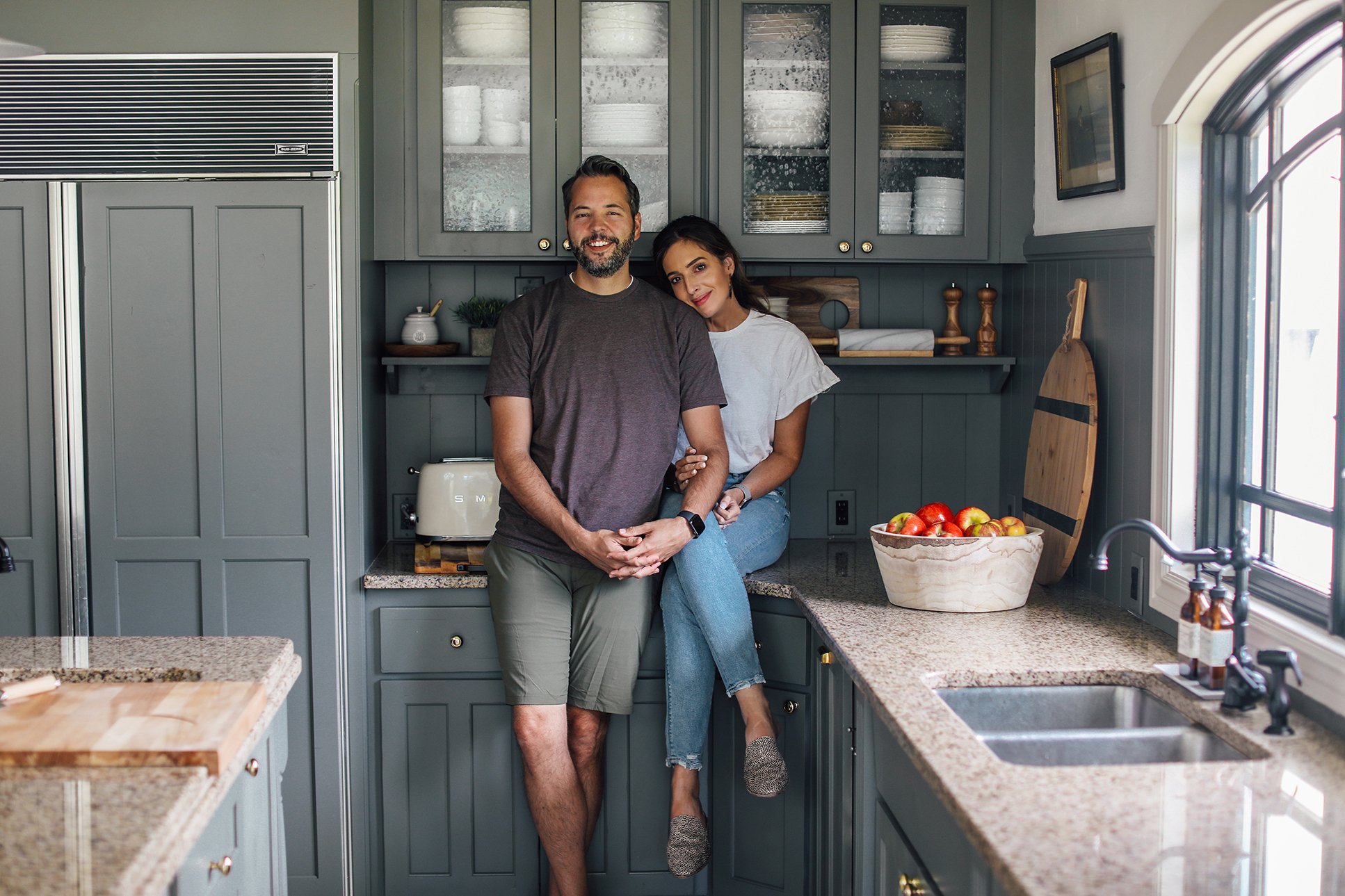 A couple standing in a softly lit kitchen at night, one partner looking overwhelmed while the other listens calmly
