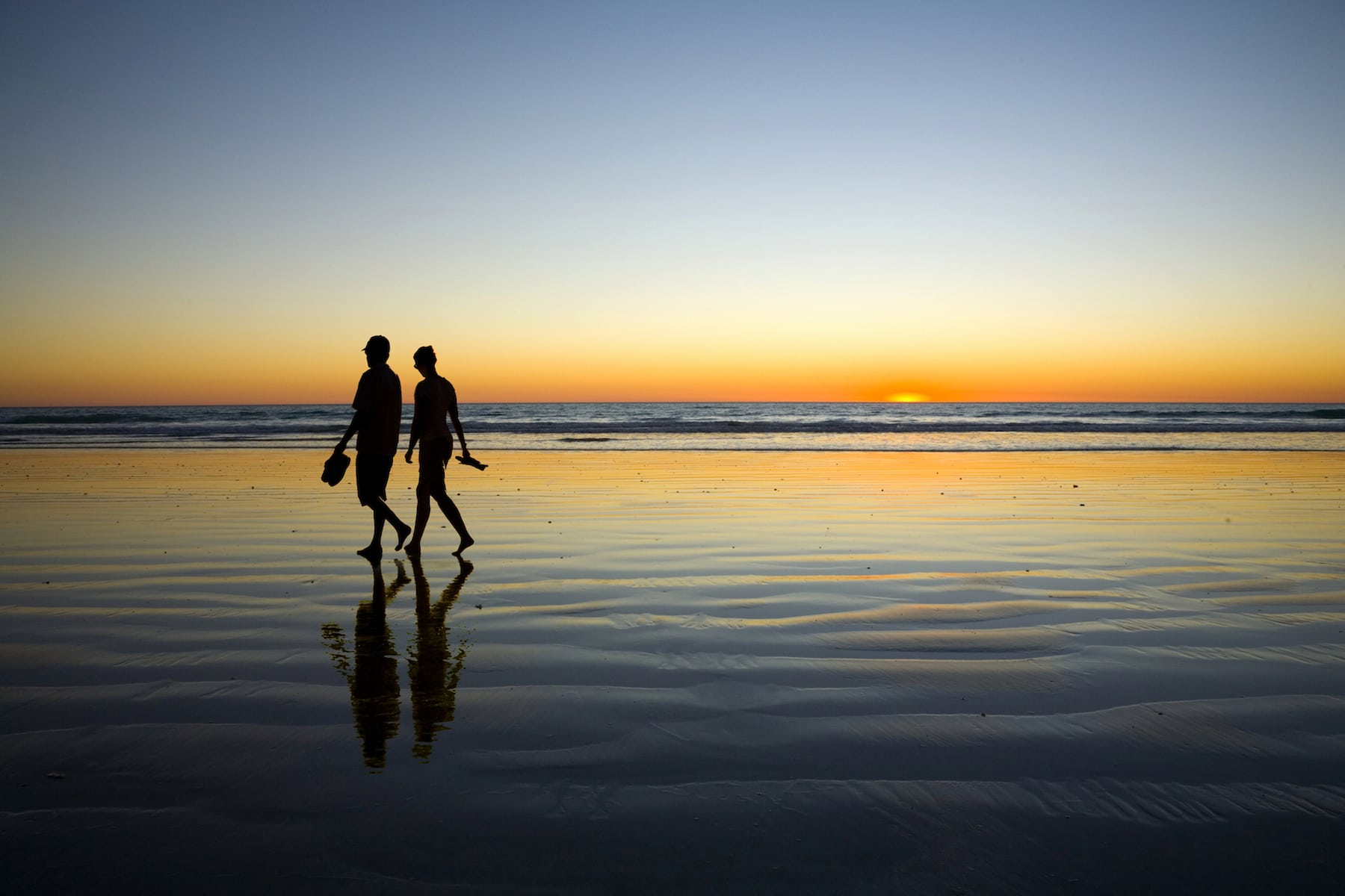 A couple walking side by side on a quiet neighborhood sidewalk at sunset, shoulders close and relaxed