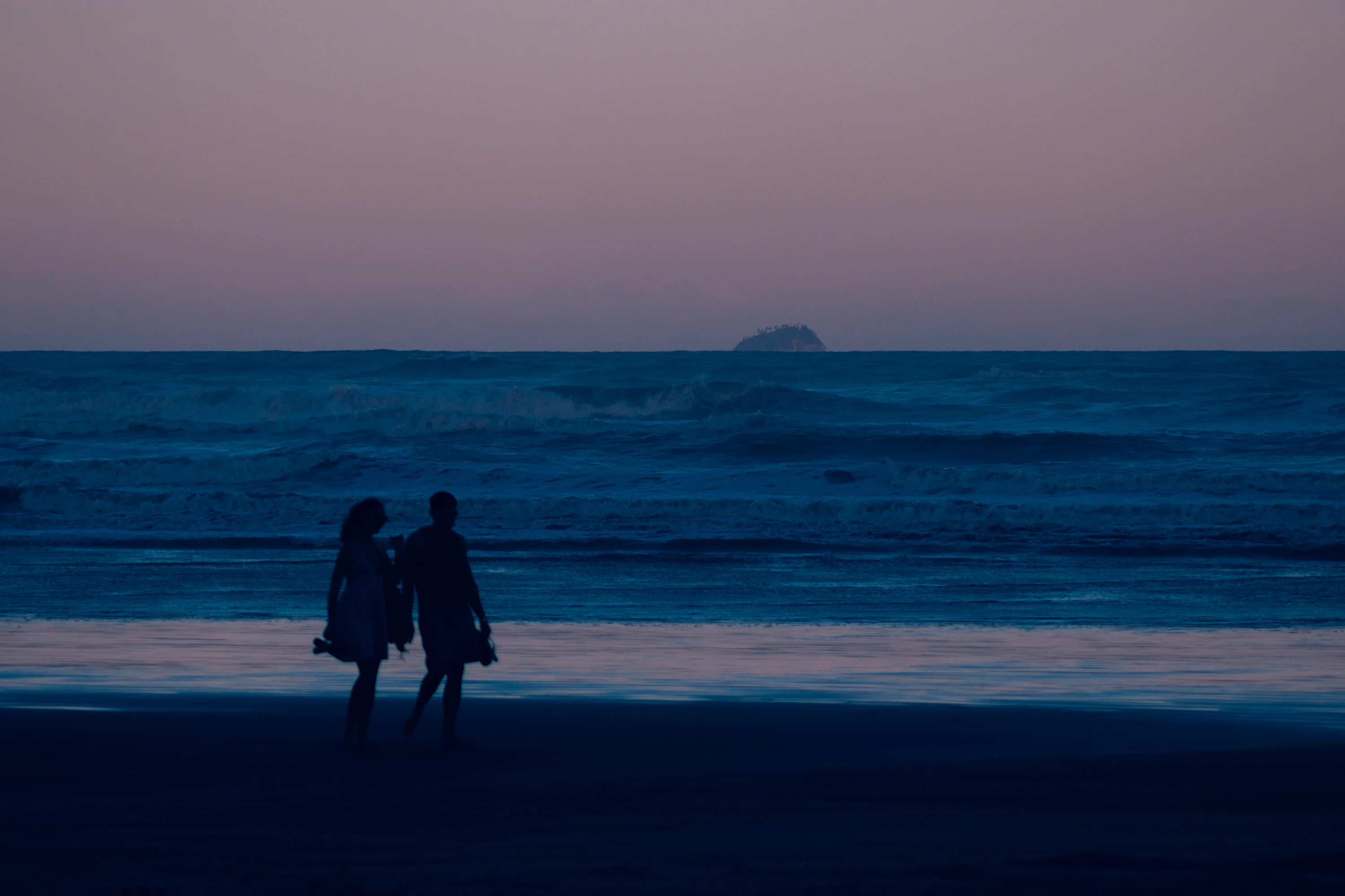 A couple walking slowly down a quiet neighborhood street at dusk, close enough to feel connected but not talking