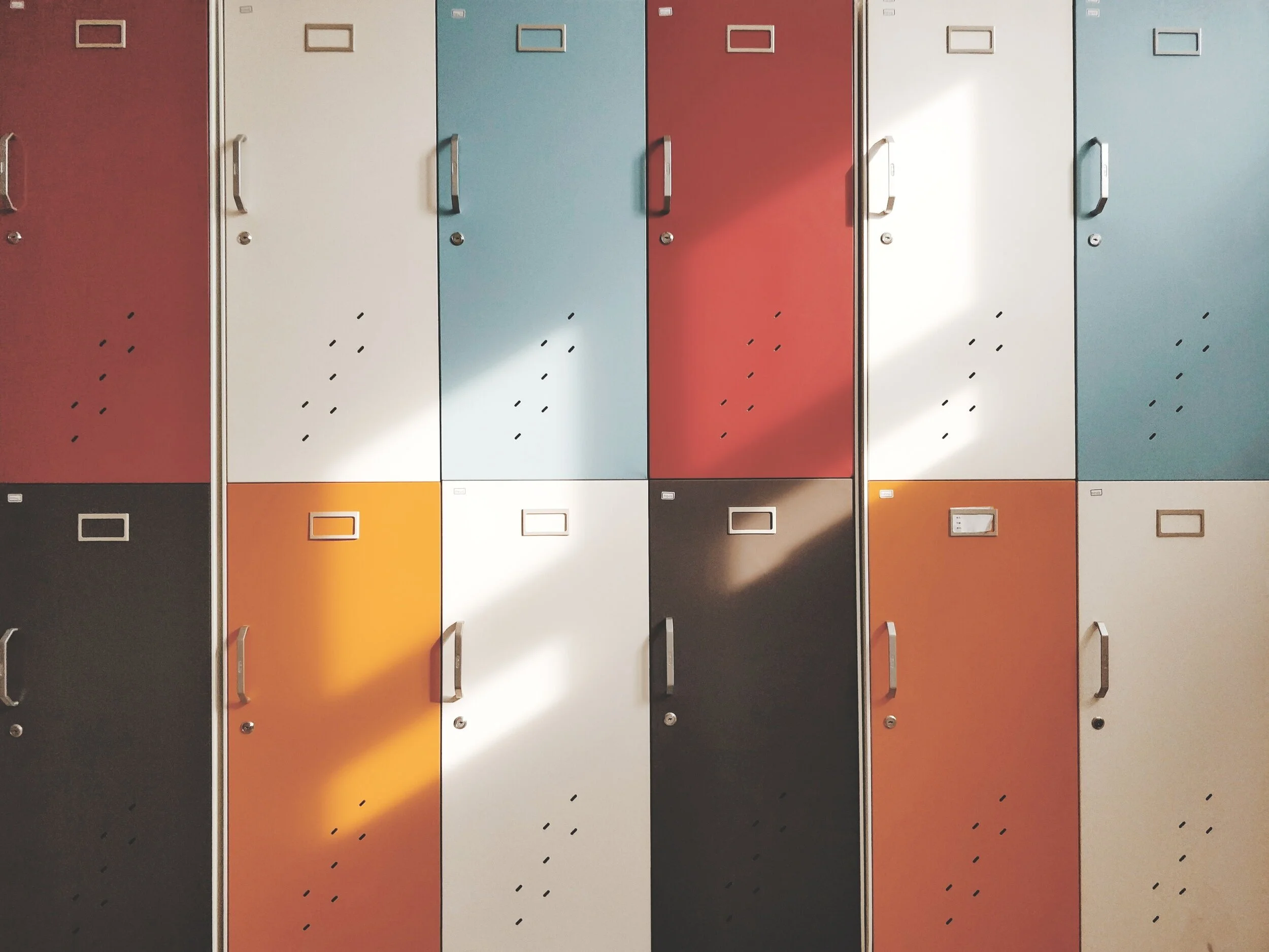 A middle school student standing alone at an open locker in a school hallway while other students walk past