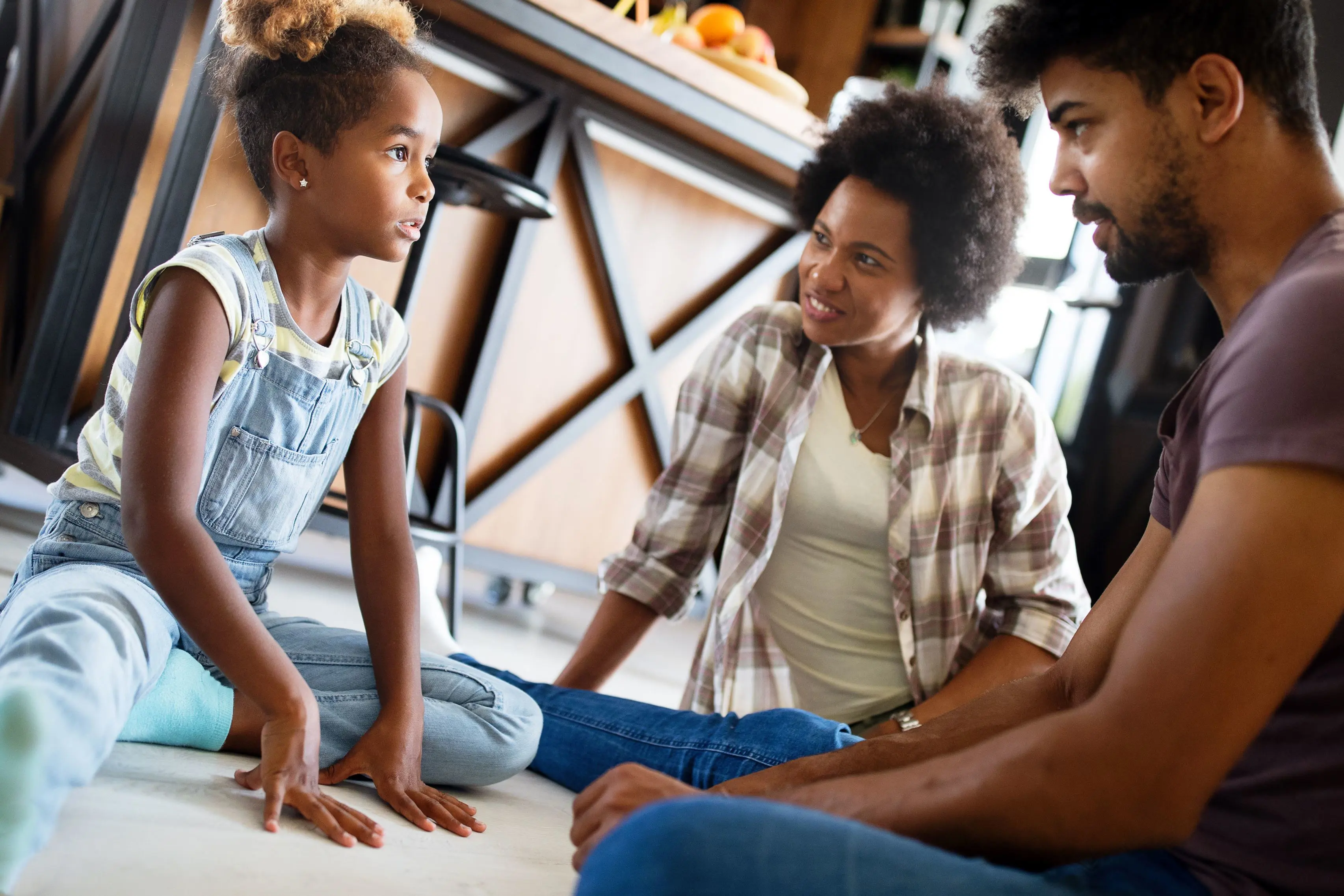 A parent and child sitting at a kitchen table having a serious, supportive conversation in warm evening light
