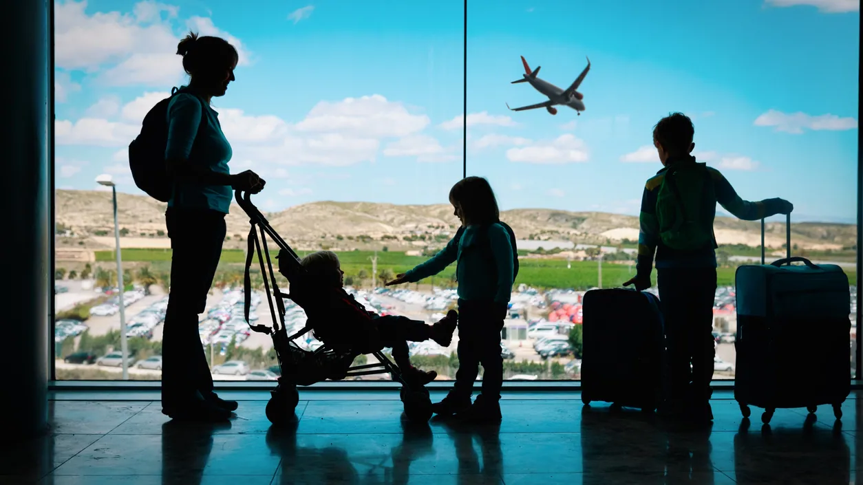 A parent holding a child’s hand while walking through an airport terminal with a small suitcase during holiday travel