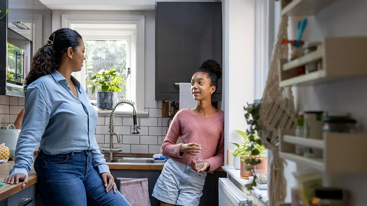 A parent holds a written list of house rules in the kitchen while an adult child listens calmly.