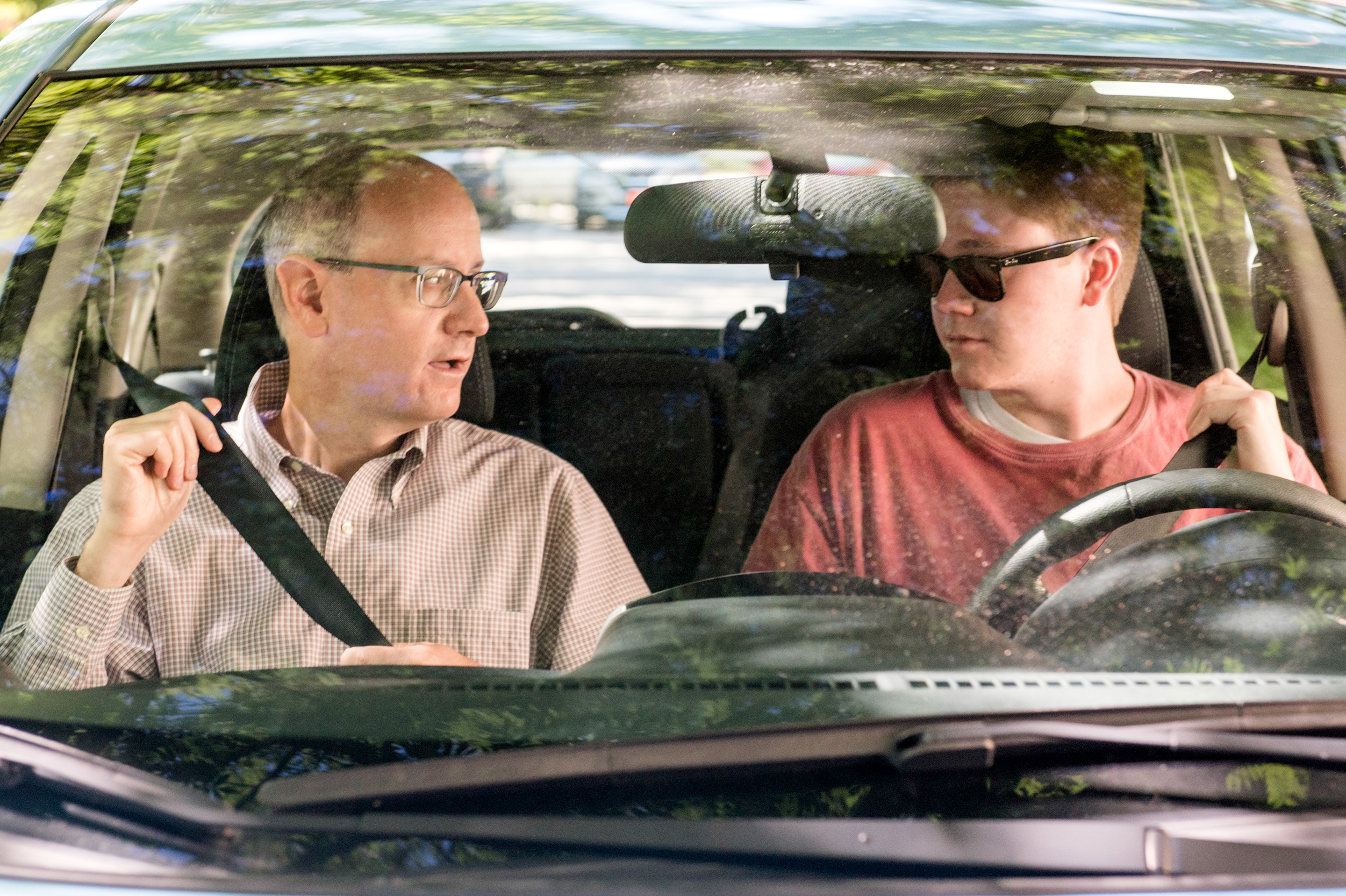 A teenager rides in the passenger seat while a parent drives. Both look forward and talk quietly.